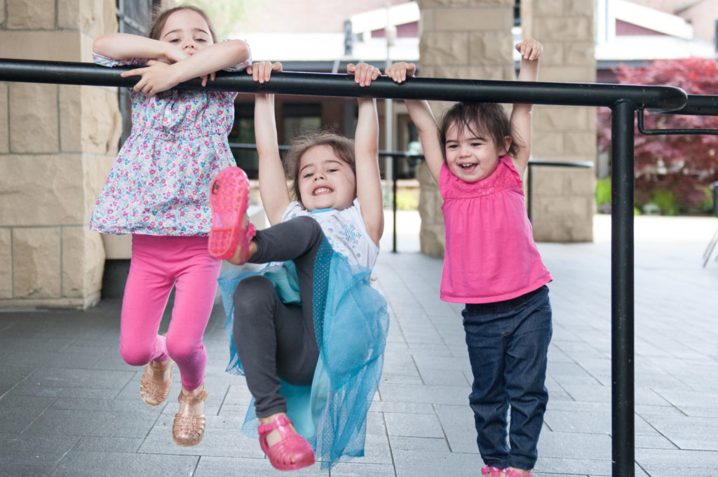 Three daughters swinging on the hand railing at the mall