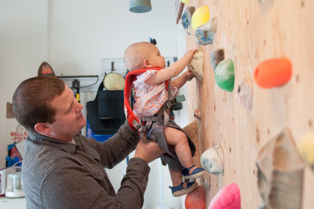 Dad holding Emma as she climbs the homemade rock wall in the garage