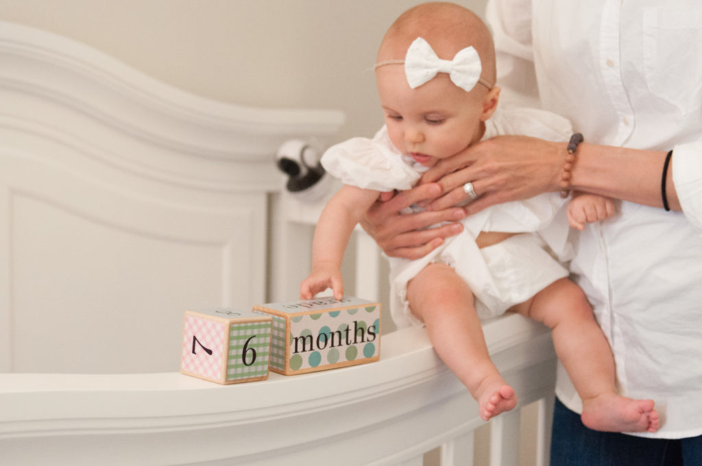 Emma's 6 month session where she is sitting on her crib holding blocks that say 6 months