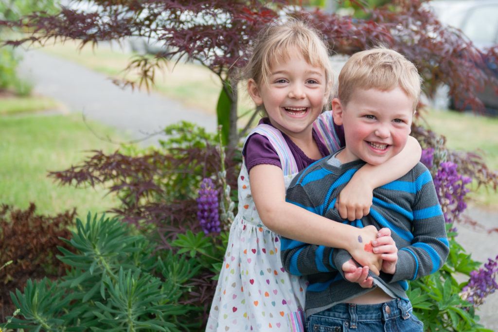 Older sister hugging her brother from behind during a backyard family session