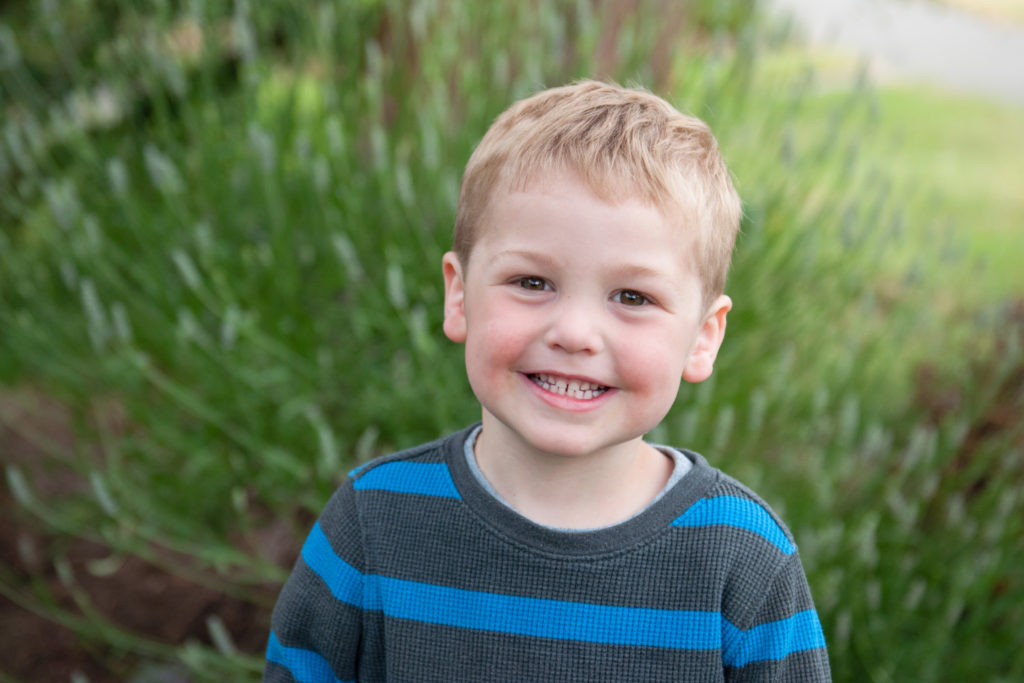 Little boy in a striped jacket smiling big during a Seattle backyard family session