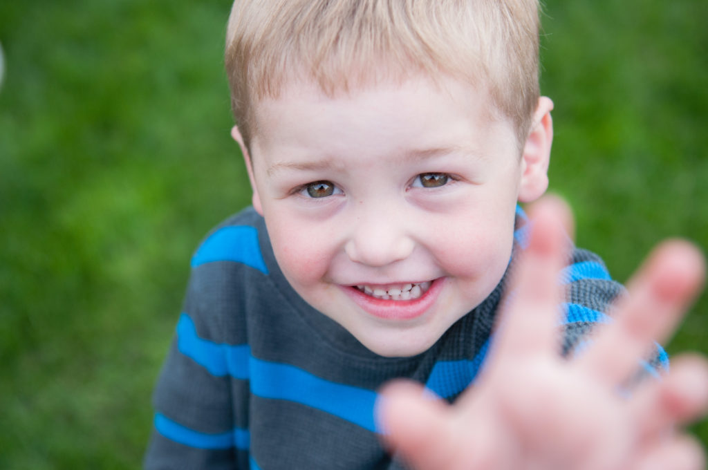 Little boy in a striped jacket reaching up for the camera to take a photo