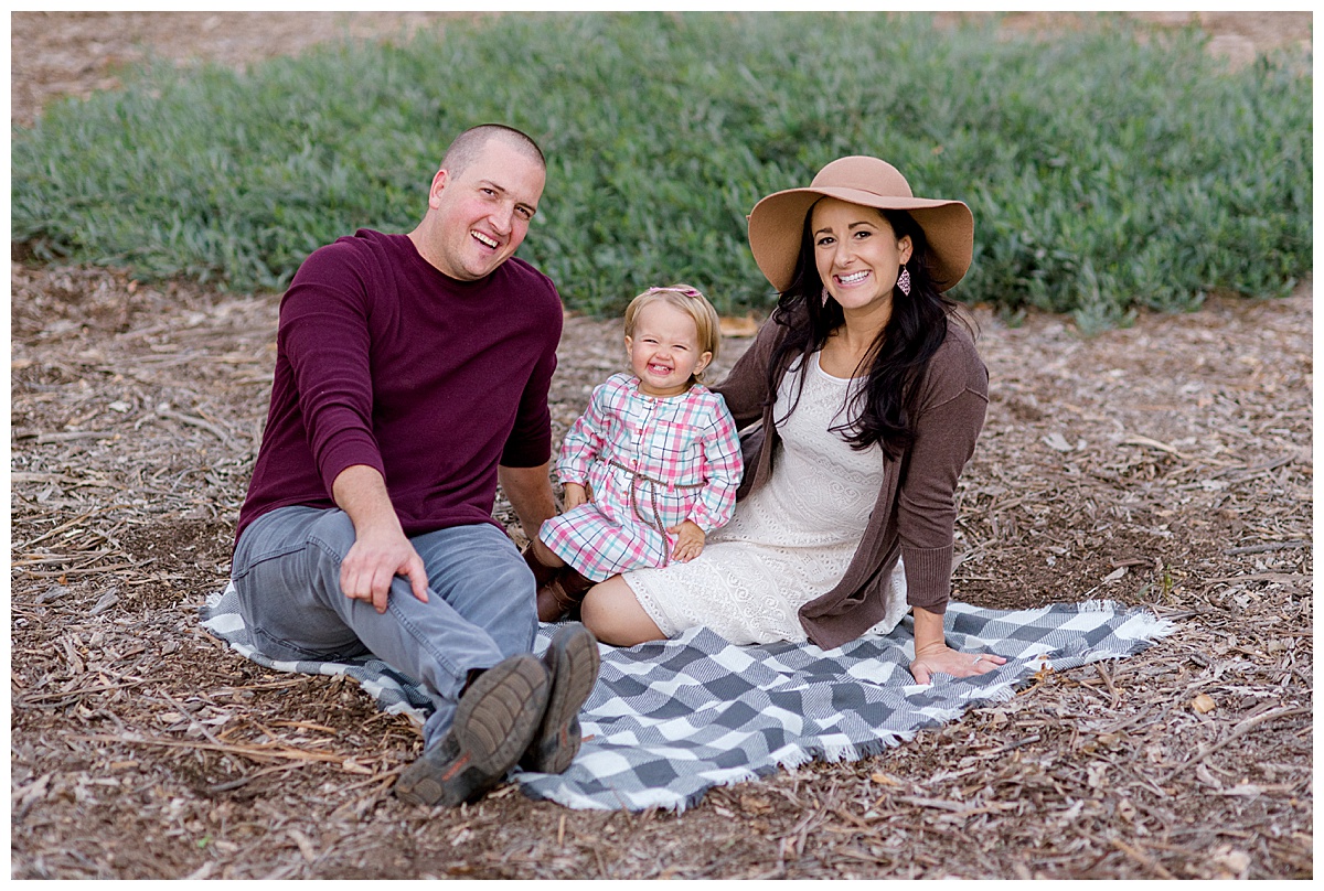 mom dad and daughter sitting on picnic blanket smiling at the camera